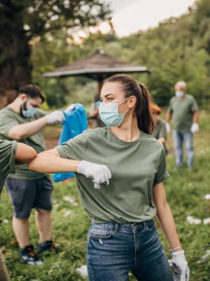 Group of people, cleaning together in public park, saving the environment together, all of them are wearing surgical masks do to coronavirus.
